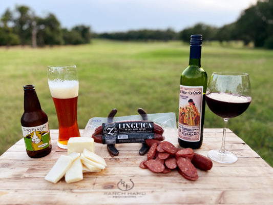 Linguica and cheese sit on a cutting board along with a wine and beer pairing.